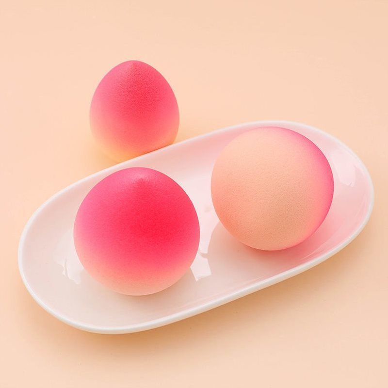 Gradient pink makeup sponge eggs on a white tray for seamless beauty application.